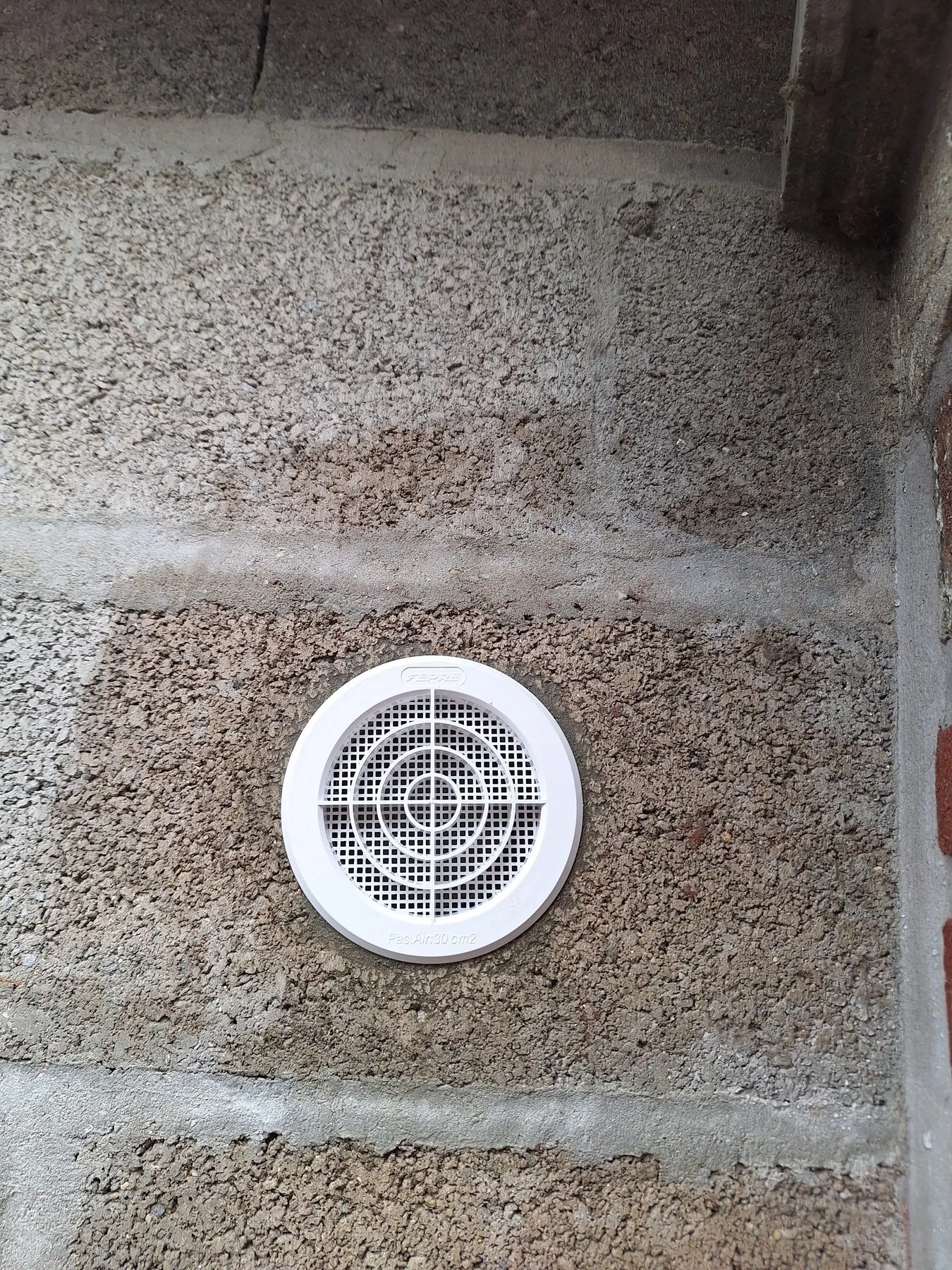 Grille d'aération ronde posée dans un mur pour l'évacuation d'un sèche-linge